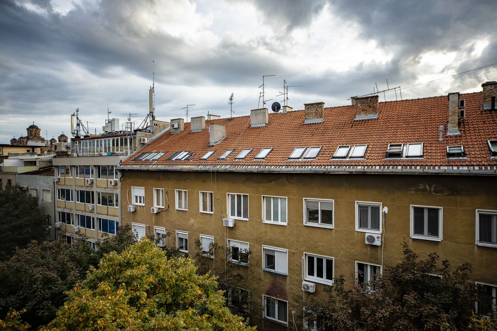Miejskie budynki z czerwonymi dachami i antenami pod burzowym niebem
