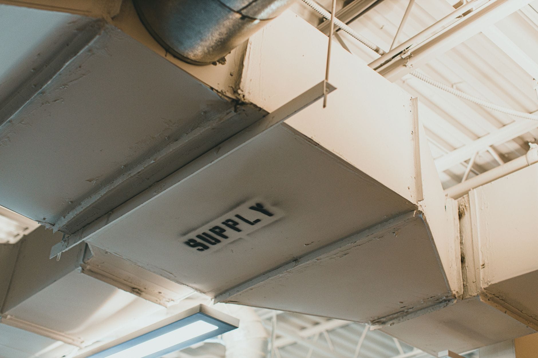 Zbliżenie na stalowy kanał wentylacyjny SUPPLY w hali przemysłowej Zbliżenie na stalowy kanał wentylacyjny SUPPLY w hali przemysłowej